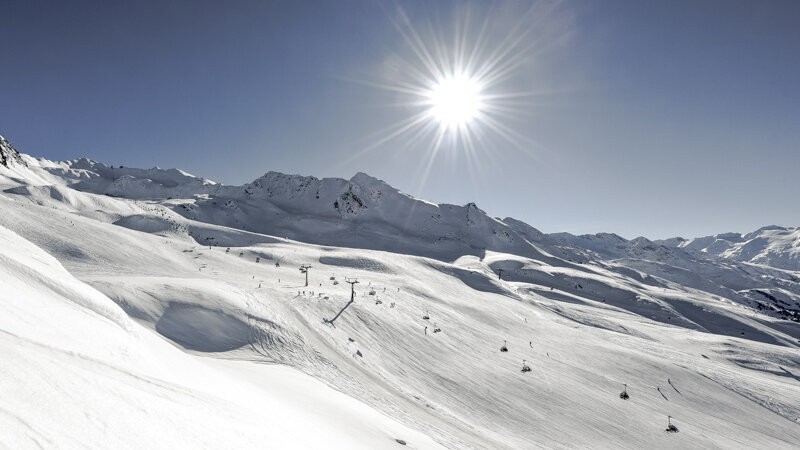 Sonniger Wintertag im Skigebiet mit breiten, verschneiten Pisten, Sesselliften und Bergkulisse unter klarem Himmel.
